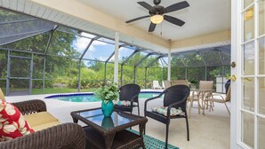 Eine überdachte Terrasse mit Pool, Korbmöbeln und Deckenventilator.