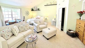 A spacious living room with a sofa set, ottoman, and coffee table. There is a dining area with a table and chairs, and a kitchen area with a counter and cabinets. - Resort-Style Studio on the Golf Course! (Conroe)