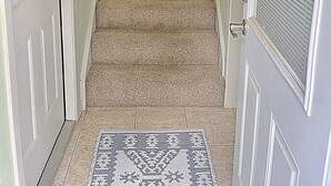 A carpeted staircase with a handrail, a patterned rug at the bottom, and a door on the left. - Private Studio Retreat on the Golf Course (Conroe)