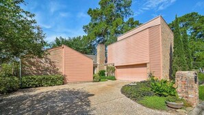 A two-story house with a brick chimney, a gravel driveway, and a well-maintained garden with various plants and flowers. - Resort-Style Studio on the Golf Course! (Conroe)