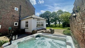 A hot tub in a backyard with a brick house, a small white building, and a garden. - Luxury Farmhouse:Padel court/Hot tub/pool table/fire pit. Central meet up point. (SELBY)