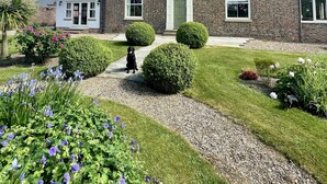 A two-story brick house with a front door, windows, and a well-maintained garden with flowers and shrubs. - Luxury Farmhouse:Padel court/Hot tub/pool table/fire pit. Central meet up point. (SELBY)