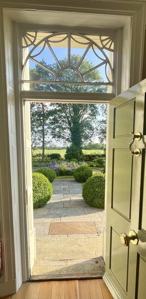 An open door leading to a stone pathway surrounded by greenery. - Luxury Farmhouse:Padel court/Hot tub/pool table/fire pit. Central meet up point. (SELBY)