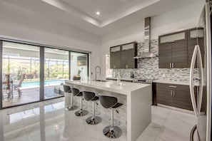 Una cocina moderna con una isla grande, taburetes de bar y vista a una piscina.