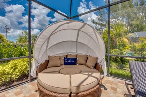 Un área de estar circular al aire libre con toldo, asientos acolchados y vistas a la vegetación circundante y la piscina.
