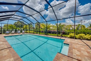 Una piscina techada con sillas de descanso y vistas de la vegetación y casas circundantes.