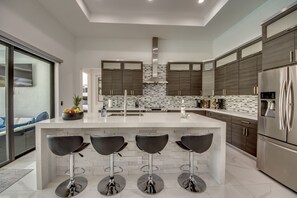 Una cocina moderna con una isla central, taburetes de bar, electrodomésticos de acero inoxidable y salpicadero de azulejos.