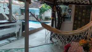 Una hamaca colgada sobre un patio con baldosas y una piscina al fondo.