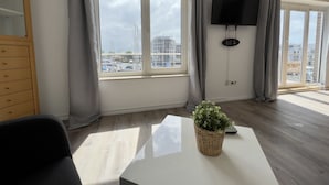 Ein modernes Wohnzimmer mit großem Fenster, einem Flachbildfernseher und einem Blumentopf.