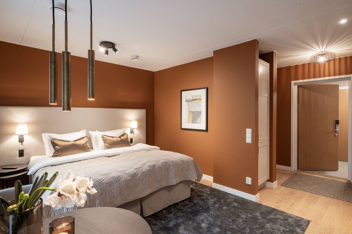 Une chambre d’hôtel moderne, dotée d’un grand lit, de lampes de chevet, d’un vase avec des fleurs et d’une porte donnant sur une autre pièce.