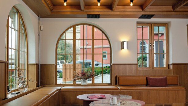 A cozy interior with a wooden bench, a round table, and large arched windows offering views of the outside. - Live and Stay - Ekmanska (Gothenburg)