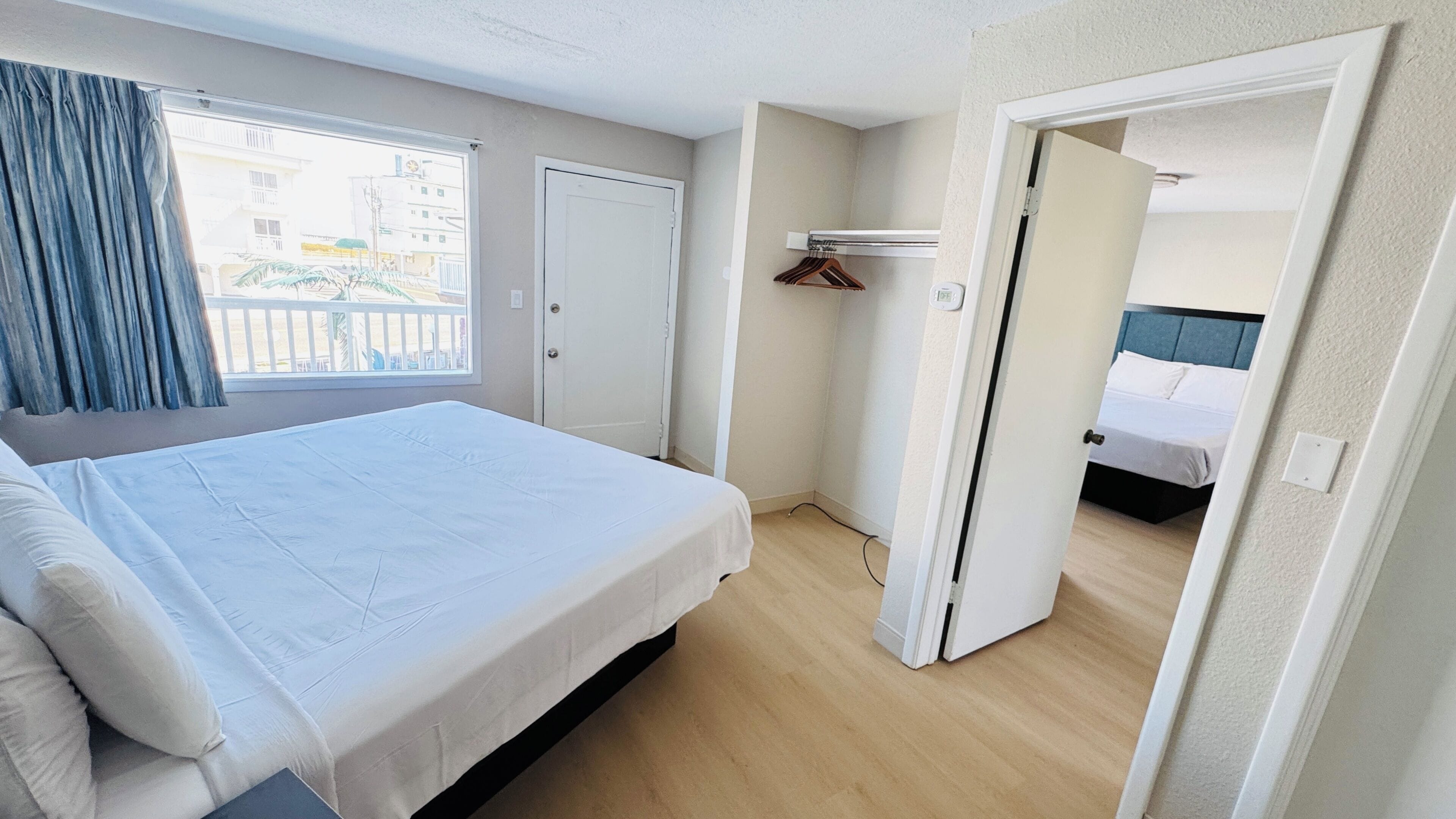 Ein Hotelzimmer mit einem großen Bett, einem Kleiderschrank, einer Tür zu einem anderen Raum und einem Fenster mit Vorhängen.