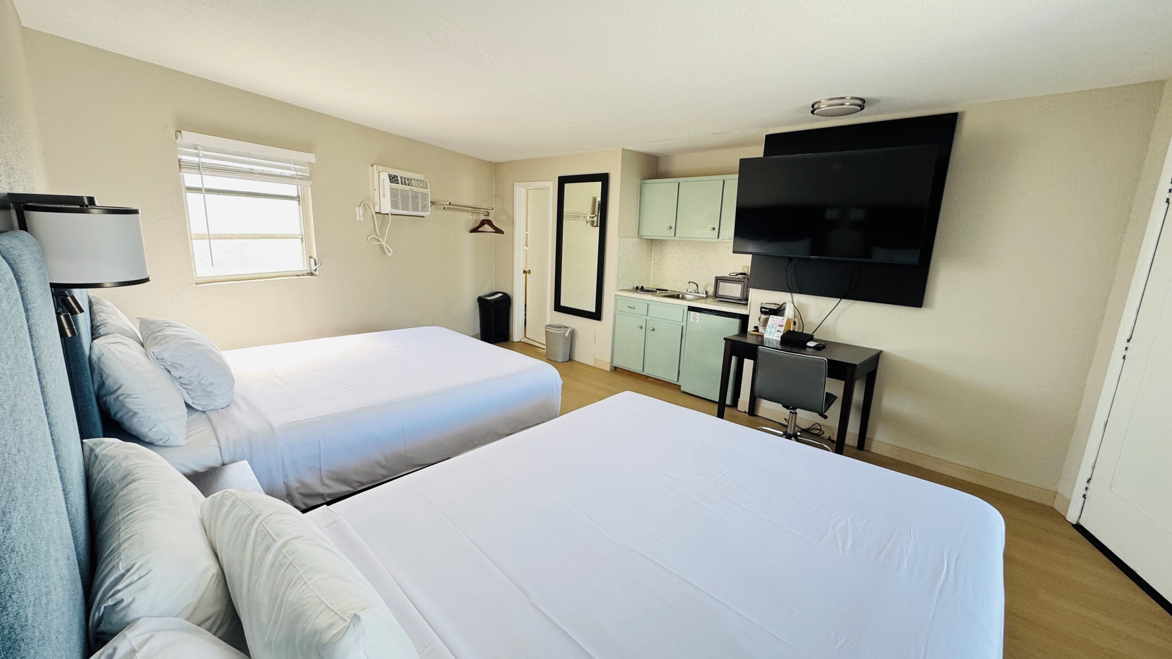 Hotelkamer met twee bedden, een bureau, een televisie, een kleine kitchenette en een raam met zonwering.