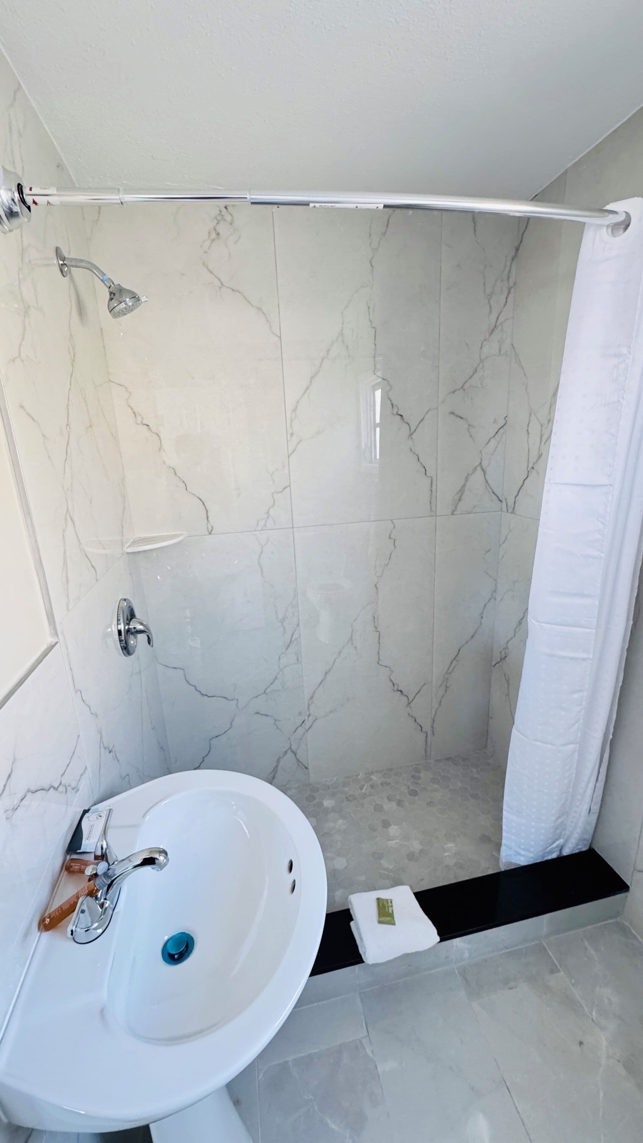 A bathroom with a shower, a sink, and a marble wall.