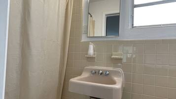 Un baño con lavabo, espejo, cortina de ducha, toallero y un cubo de basura.