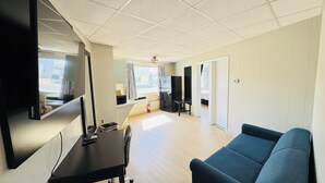 A room with a flat-screen TV, a black table, a blue sofa, a ceiling fan, and a view of the street through a window. - Bel Air Motel (Wildwood Crest)