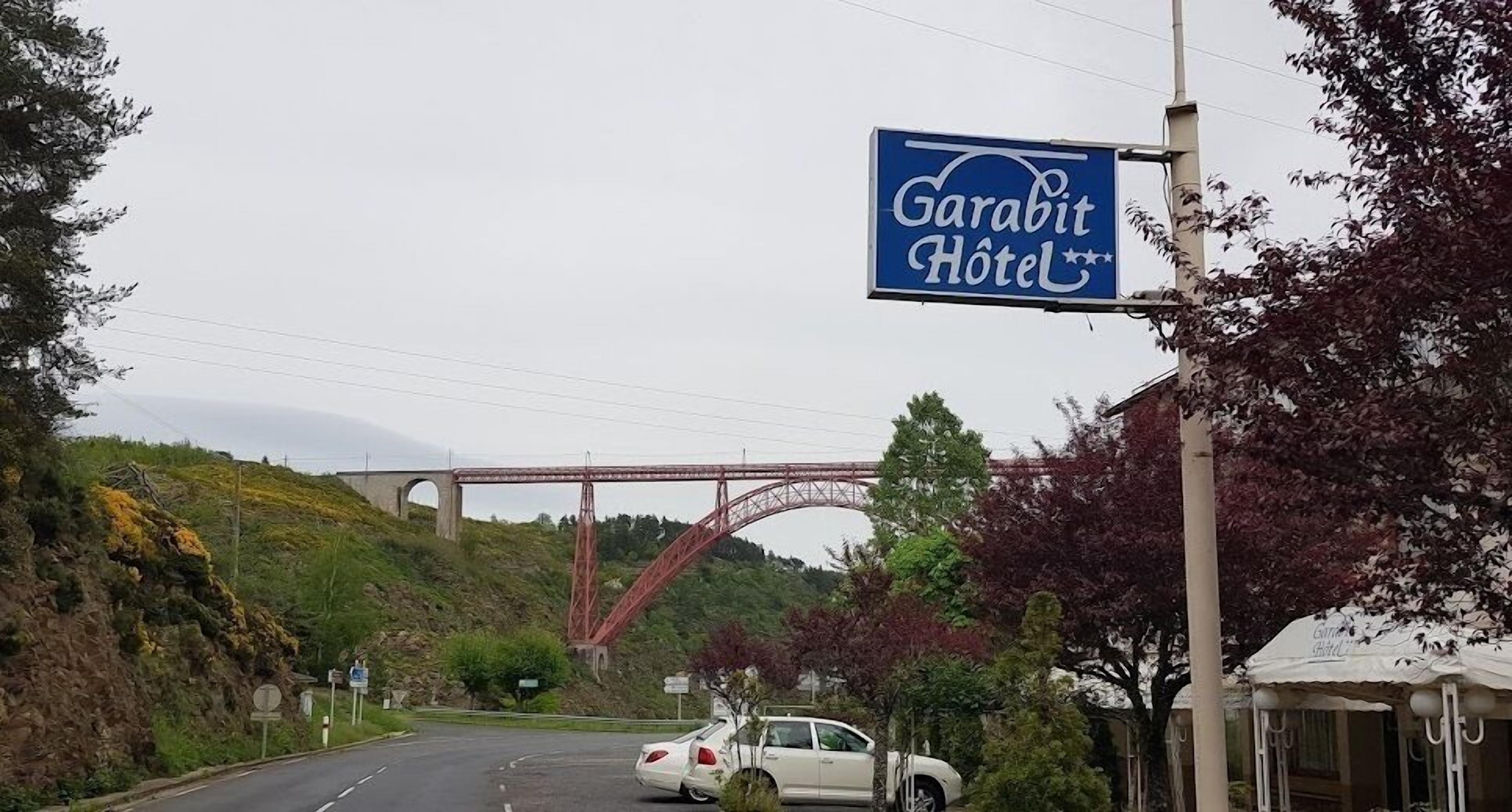 A sign for Garabit Hotel with a red bridge in the background.