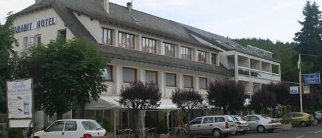 Hotel Garabit de dois andares, com fachada branca e telhado cinzento. Vários carros estão estacionados em frente, e uma placa anuncia o restaurante do hotel.