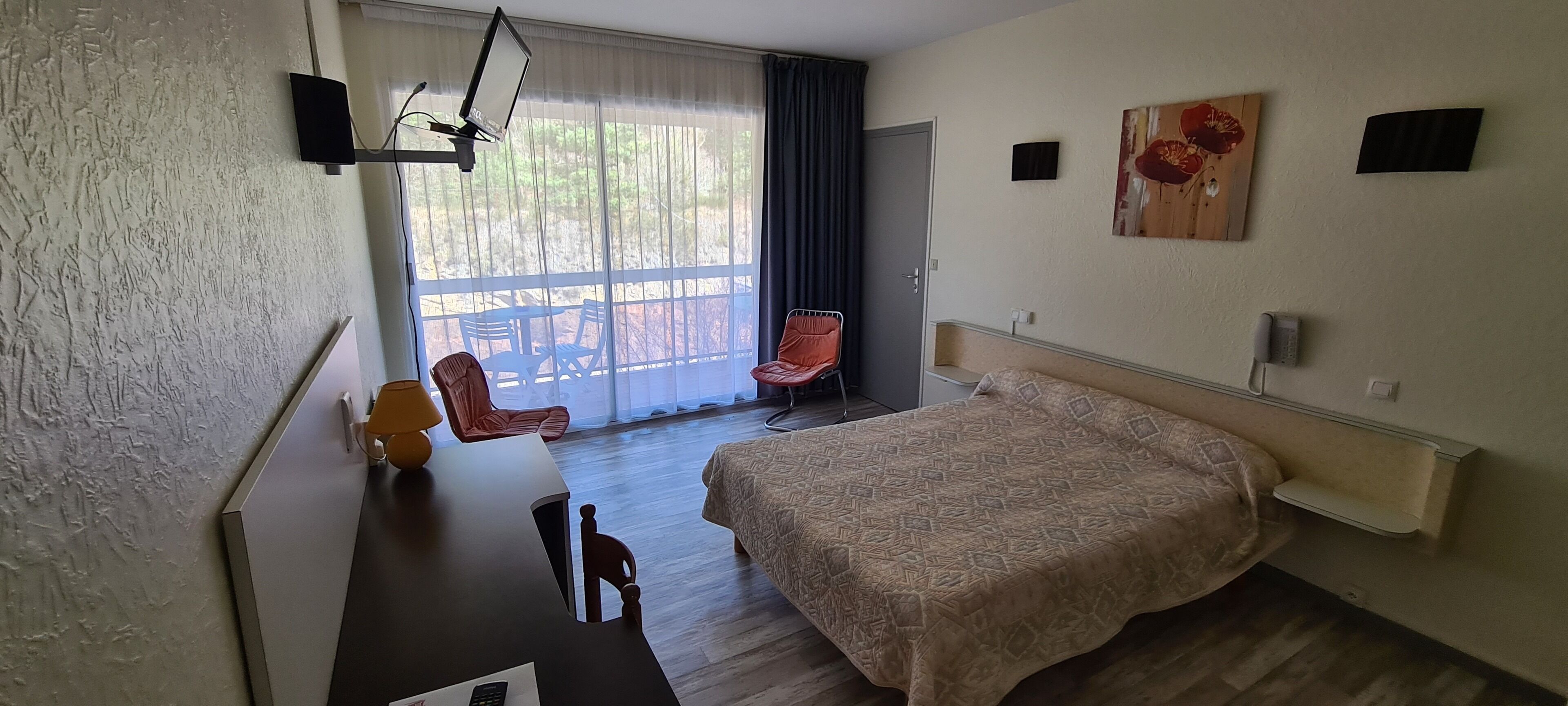 A hotel room with a bed, a desk with a lamp, a chair, a TV, and a window with curtains.