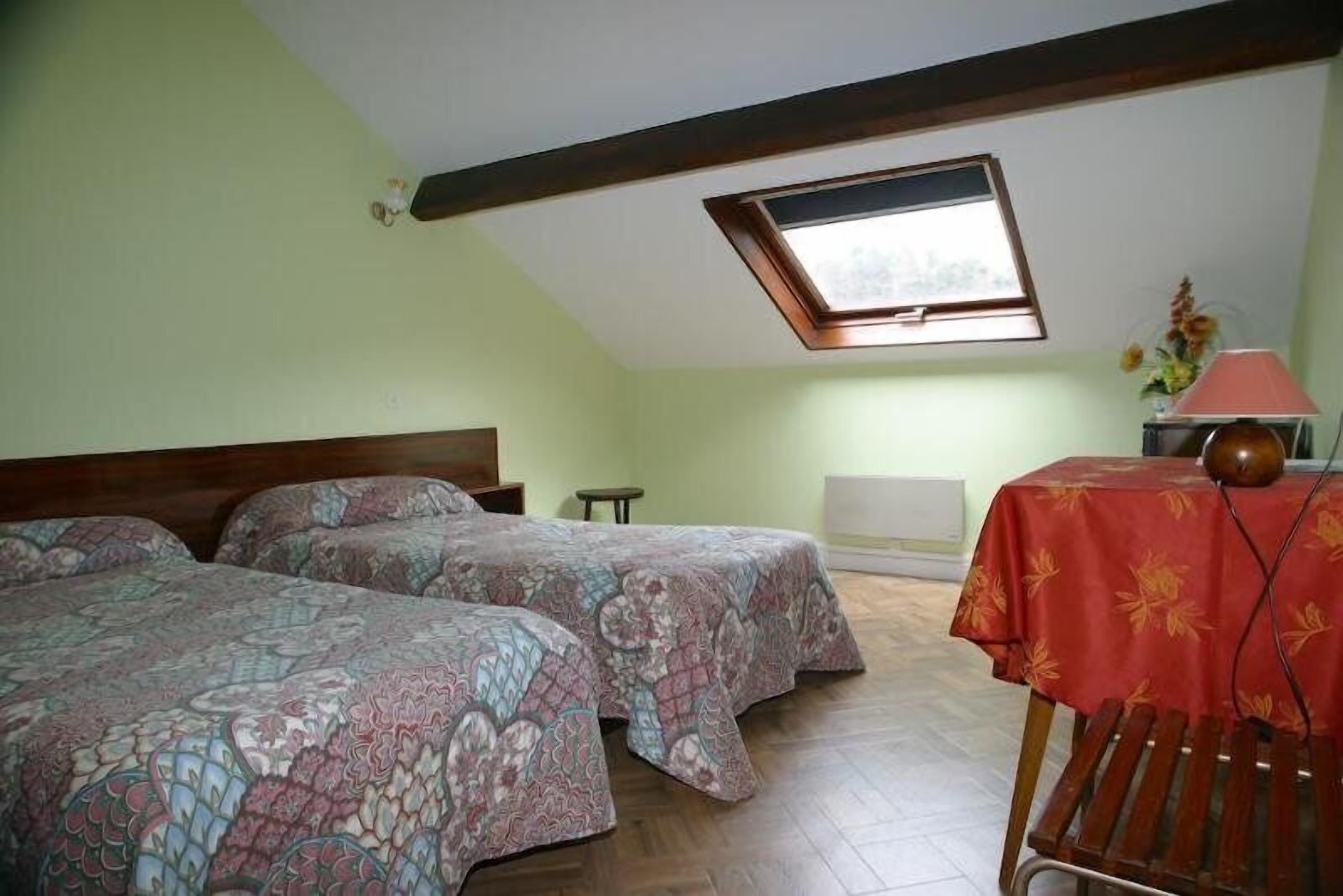 Une chambre avec deux lits, une lucarne, une petite table avec une lampe et un banc en bois.