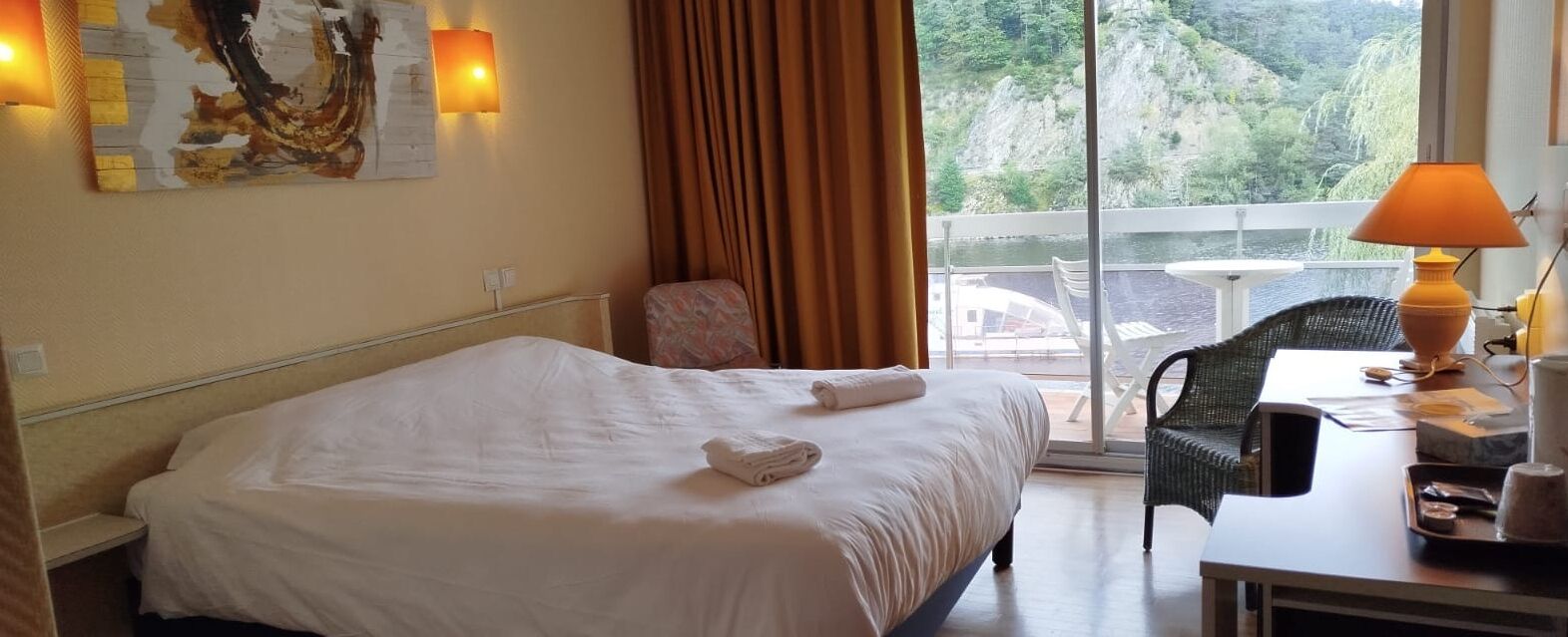 Une chambre d’hôtel avec un lit, une chaise, une table et une vue sur un balcon doté d’une balustrade.