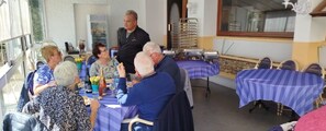 A group of people seated around a table with food and drinks, in a room with tables covered in blue tablecloths. - Garabit Hôtel (Anglards-de-Saint-Flour)