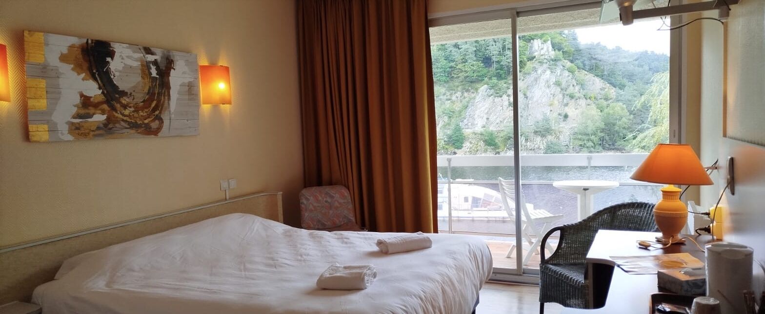 A hotel room with a bed, a chair, a table, a lamp, and a painting on the wall.