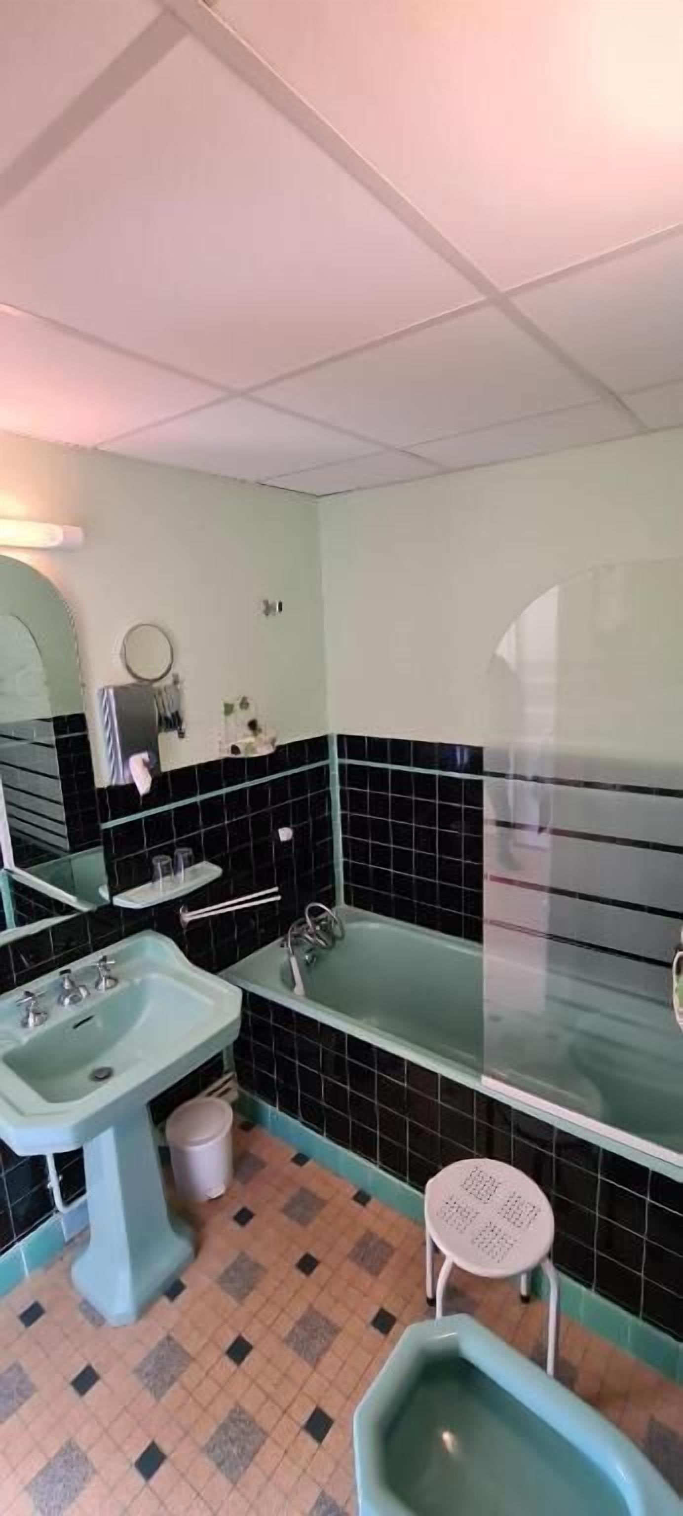 Ein Badezimmer mit Waschbecken, Toilette und Badewanne. Über dem Waschbecken hängt ein Spiegel und neben der Badewanne steht ein kleiner Hocker.