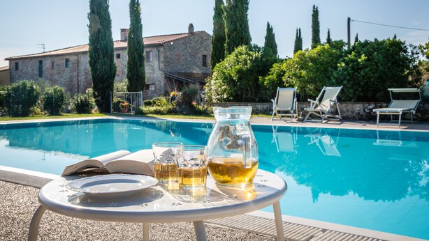A poolside setting with a table, a pitcher, and glasses, surrounded by lounge chairs and a stone building in the background. - For groups, in the heart of Tuscany 40 km from Pisa airport (Chianni)