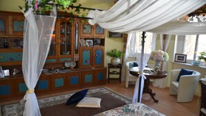 A bedroom with a canopy bed, a wooden cabinet with glass doors, a small table with a vase, and a chair. - Vacation apartment "Fritz" in the Villa Hünlich with a rondel view of Upper Lusatia (Wilthen)