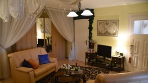 A living room with a sofa, coffee table, and TV. There is a door with a green wreath, a lamp, and a framed picture on the wall. - Vacation apartment "Fritz" in the Villa Hünlich with a rondel view of Upper Lusatia (Wilthen)