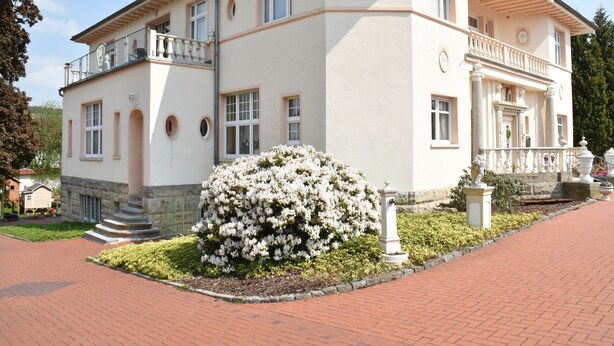 A large, two-story building with a symmetrical facade, a central entrance with columns, and a small balcony on the upper floor. - Vacation apartment "Fritz" in the Villa Hünlich with a rondel view of Upper Lusatia (Wilthen)