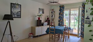 Een kamer met een eettafel, stoelen, een boekenkast, een lamp en een raam met gordijnen.