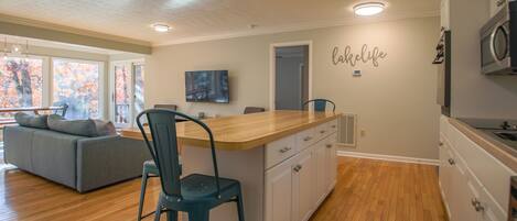 Una cocina moderna con una isla de madera, un área de comedor con un sofá y un televisor montado en la pared.