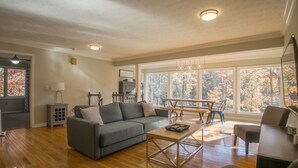 A spacious living room with a grey sofa, wooden coffee table, and a dining area with a table and chairs.