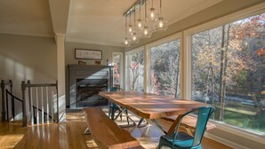 A dining area with a wooden table and benches, large windows with a view of trees, and a hanging light fixture.