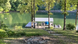 A lakeside cabin with a dock, surrounded by trees and a grassy area.