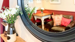 A mirror reflecting a room with a dining table, a sofa, and a vase with flowers on a shelf. - The Old Bookshop - cheerful house located in St Ives centre (St Ives)