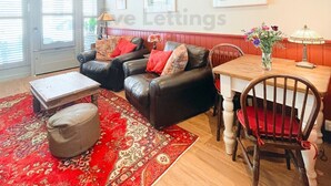A living room with a red patterned rug, leather sofas, a wooden dining table, and a chair. - The Old Bookshop - cheerful house located in St Ives centre (St Ives)