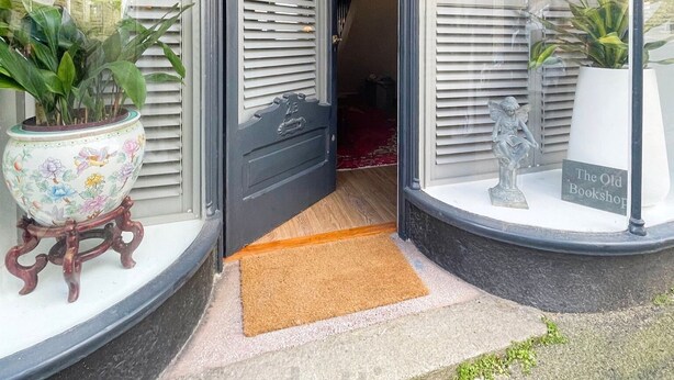 A building entrance with a black door, a doormat, and two potted plants on either side. - The Old Bookshop - cheerful house located in St Ives centre (St Ives)