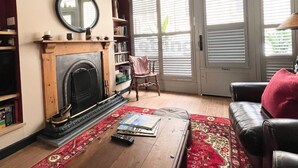 A living room with a fireplace, bookshelves, a coffee table, and a red patterned rug. - The Old Bookshop - cheerful house located in St Ives centre (St Ives)