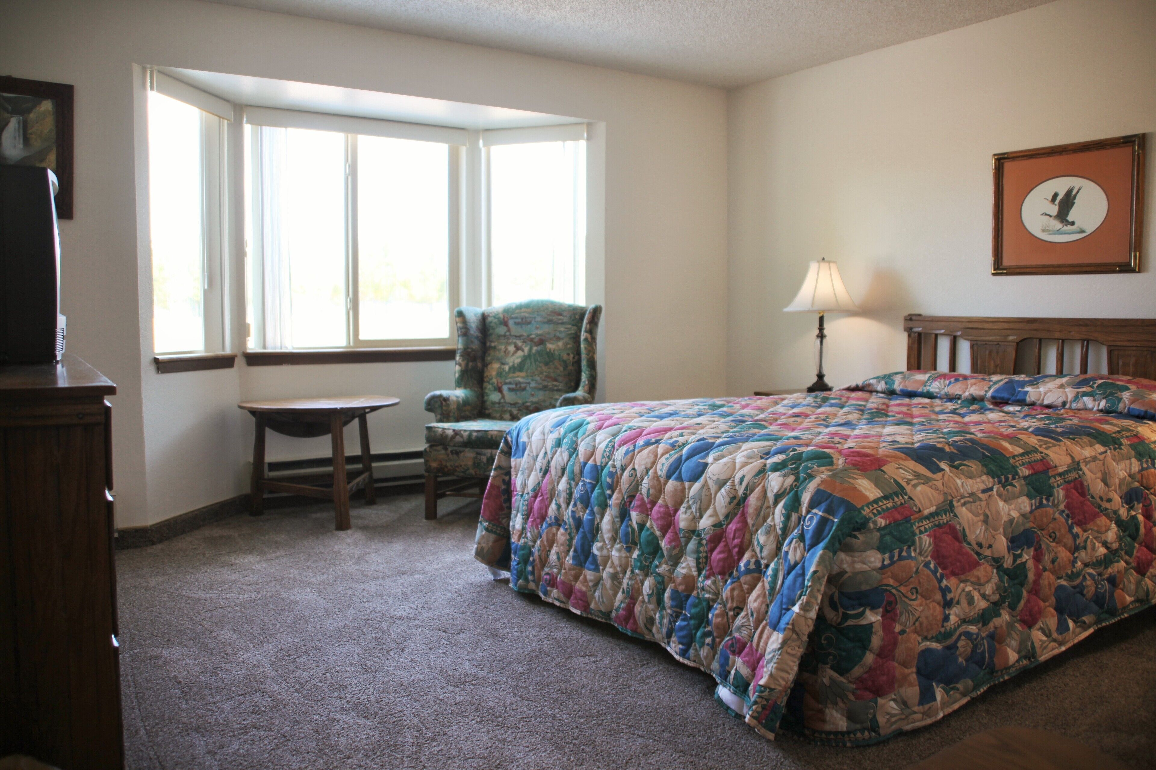 A bedroom with a large bed, a chair, a desk, and a window.