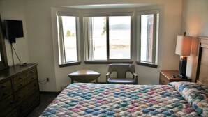 Quarto de hotel com uma cama grande, uma escrivaninha e uma cadeira. Janelas oferecem vista para o exterior.
