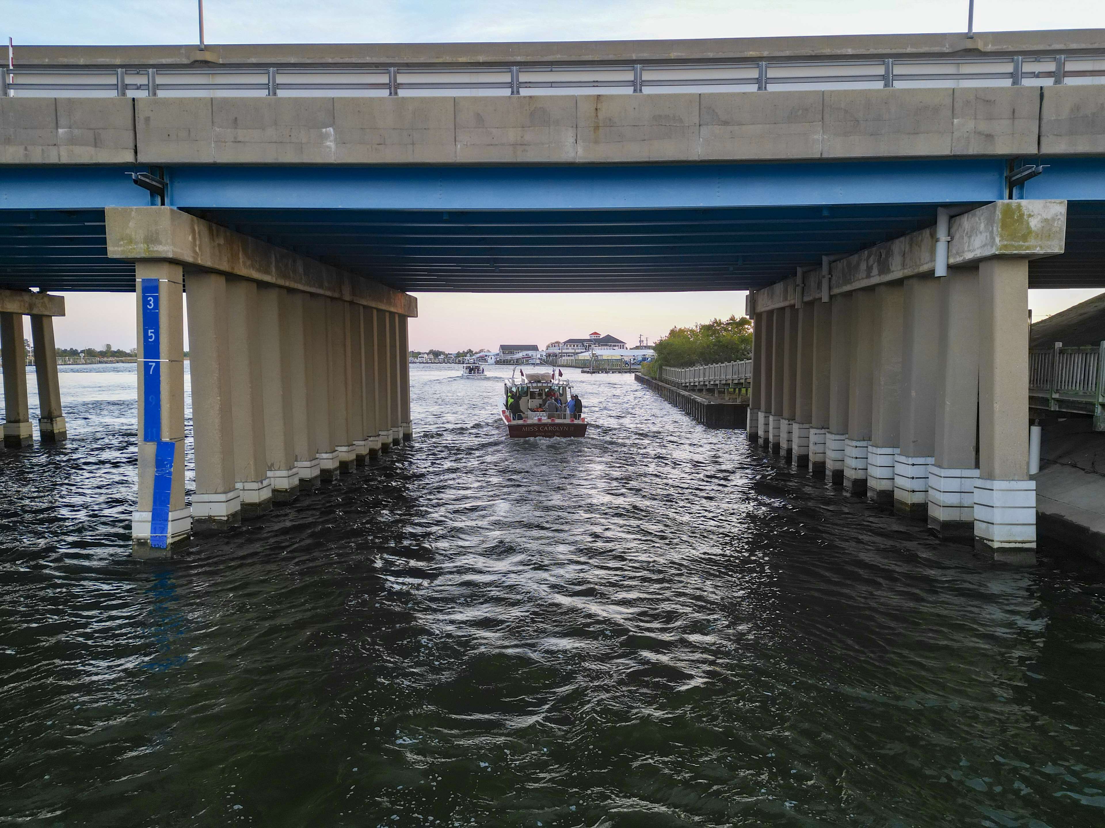 A boat named "Miss Caroline II" under a bridge with water on both sides.