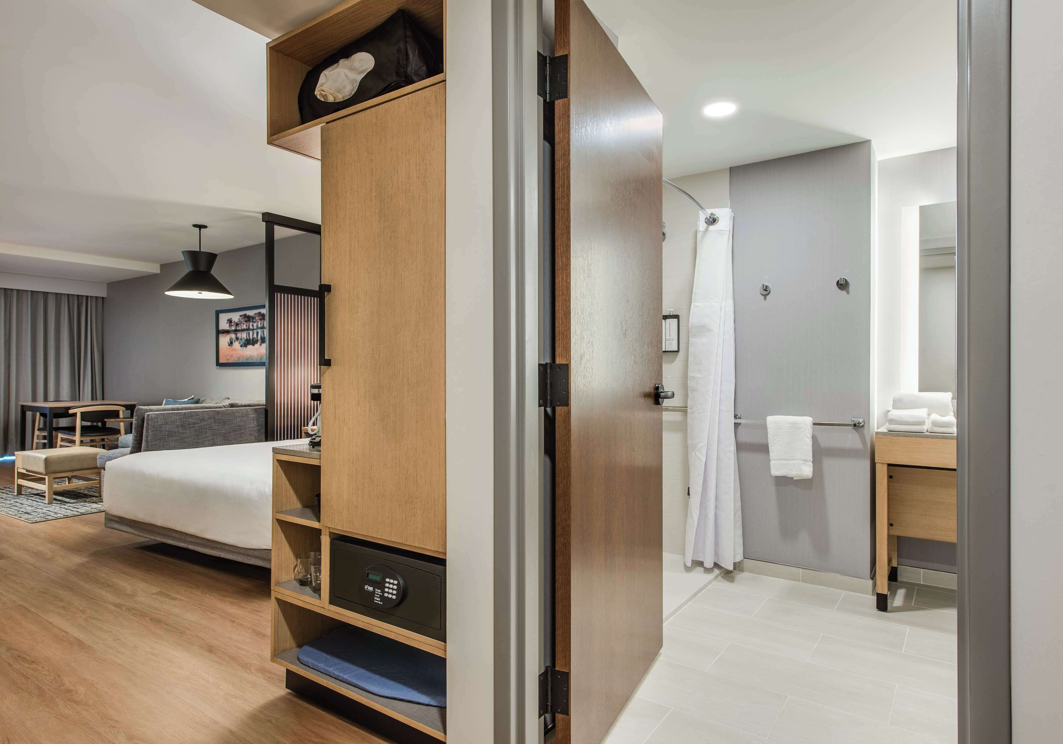 A modern hotel room with a bed, a desk, a wardrobe, and a shower area.