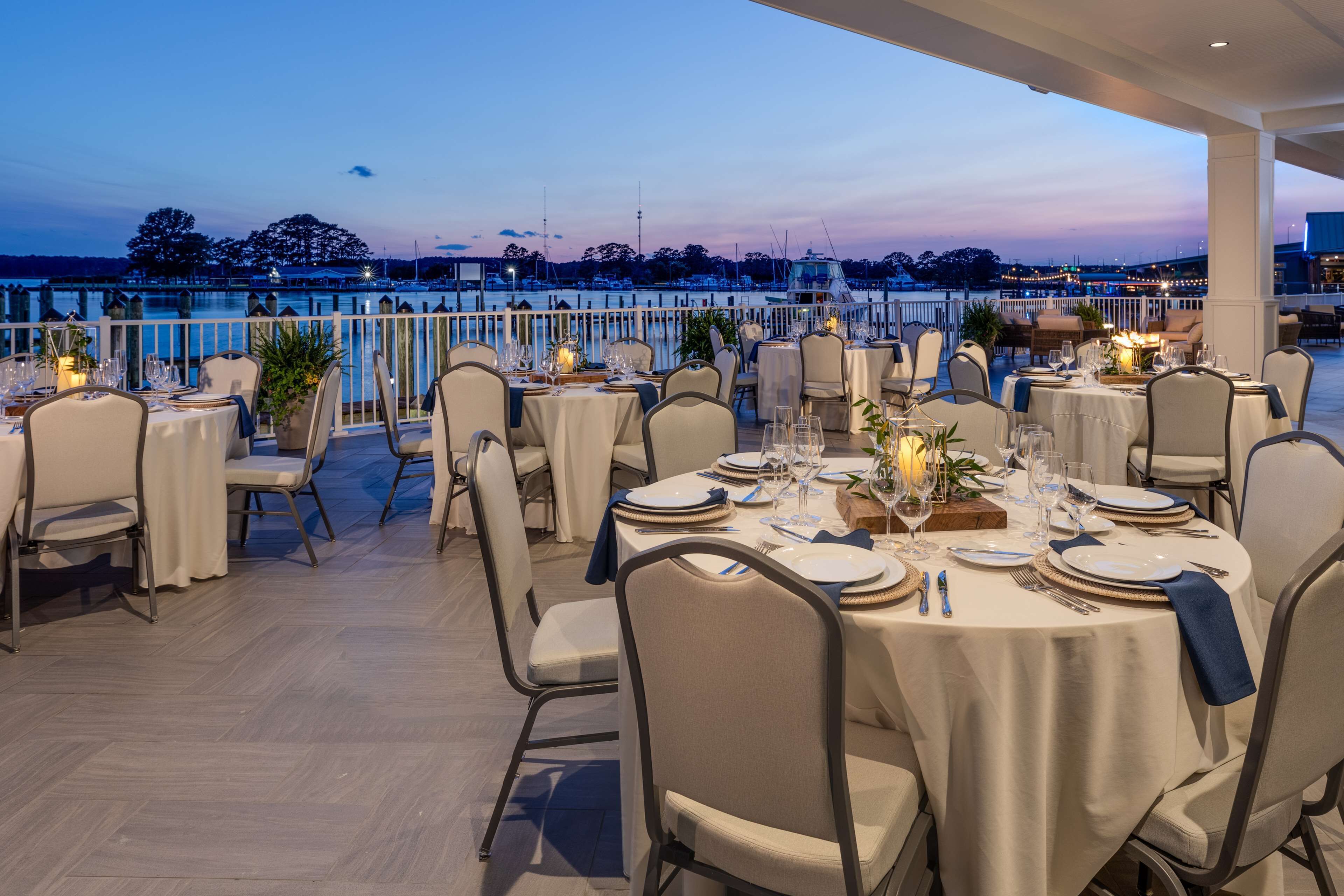 A restaurant with round tables set for dining, overlooking a marina.