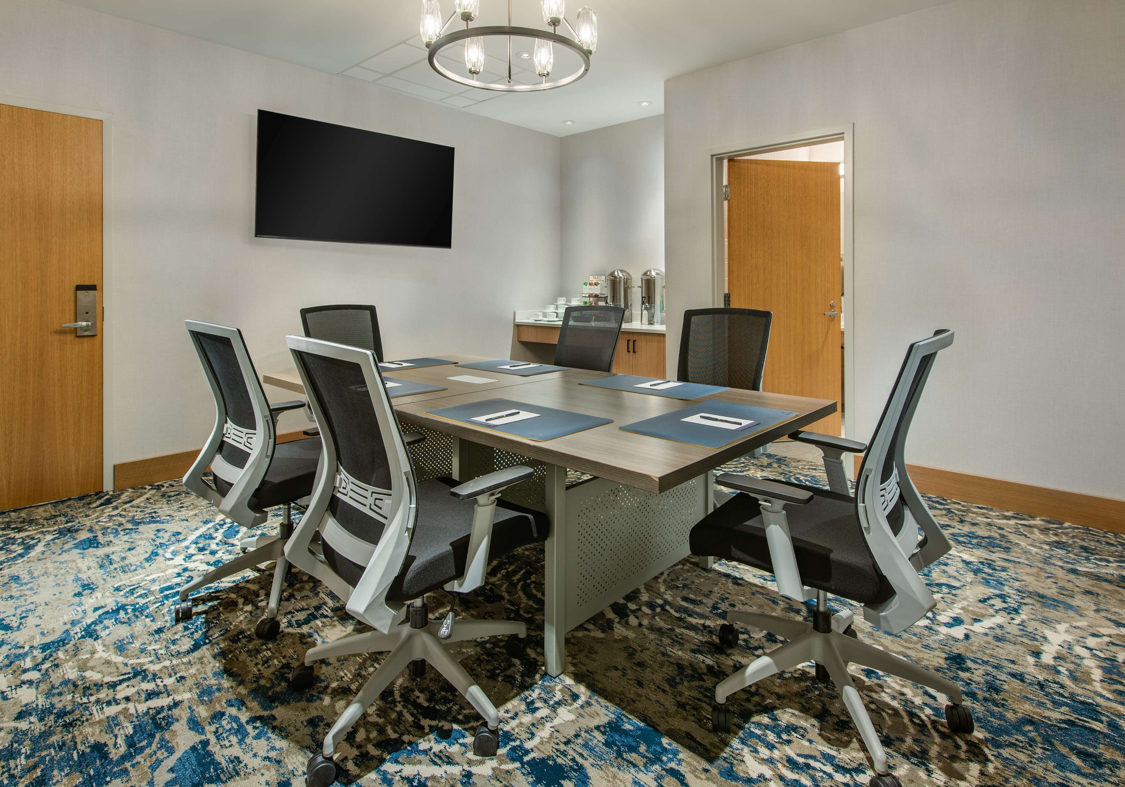A conference room with a large table, four chairs, a flat-screen TV, and a coffee station.