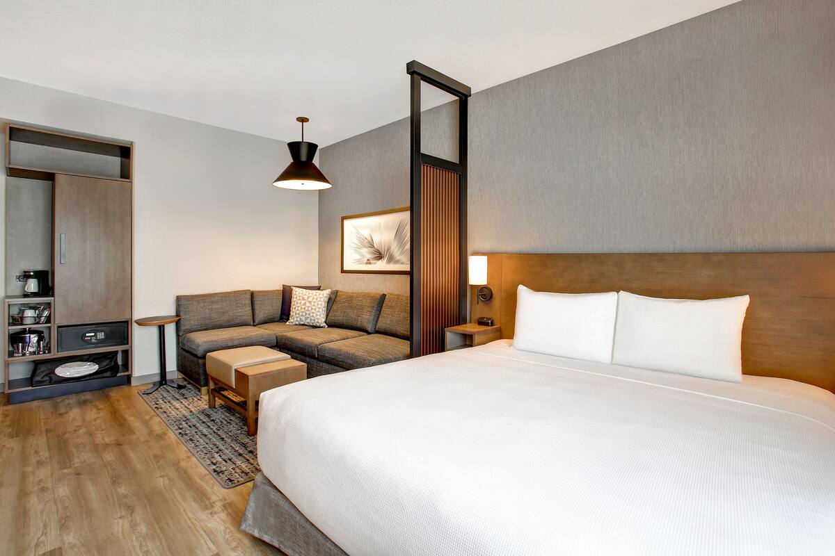 A modern hotel room with a large bed, a sofa, a desk, and a wardrobe.