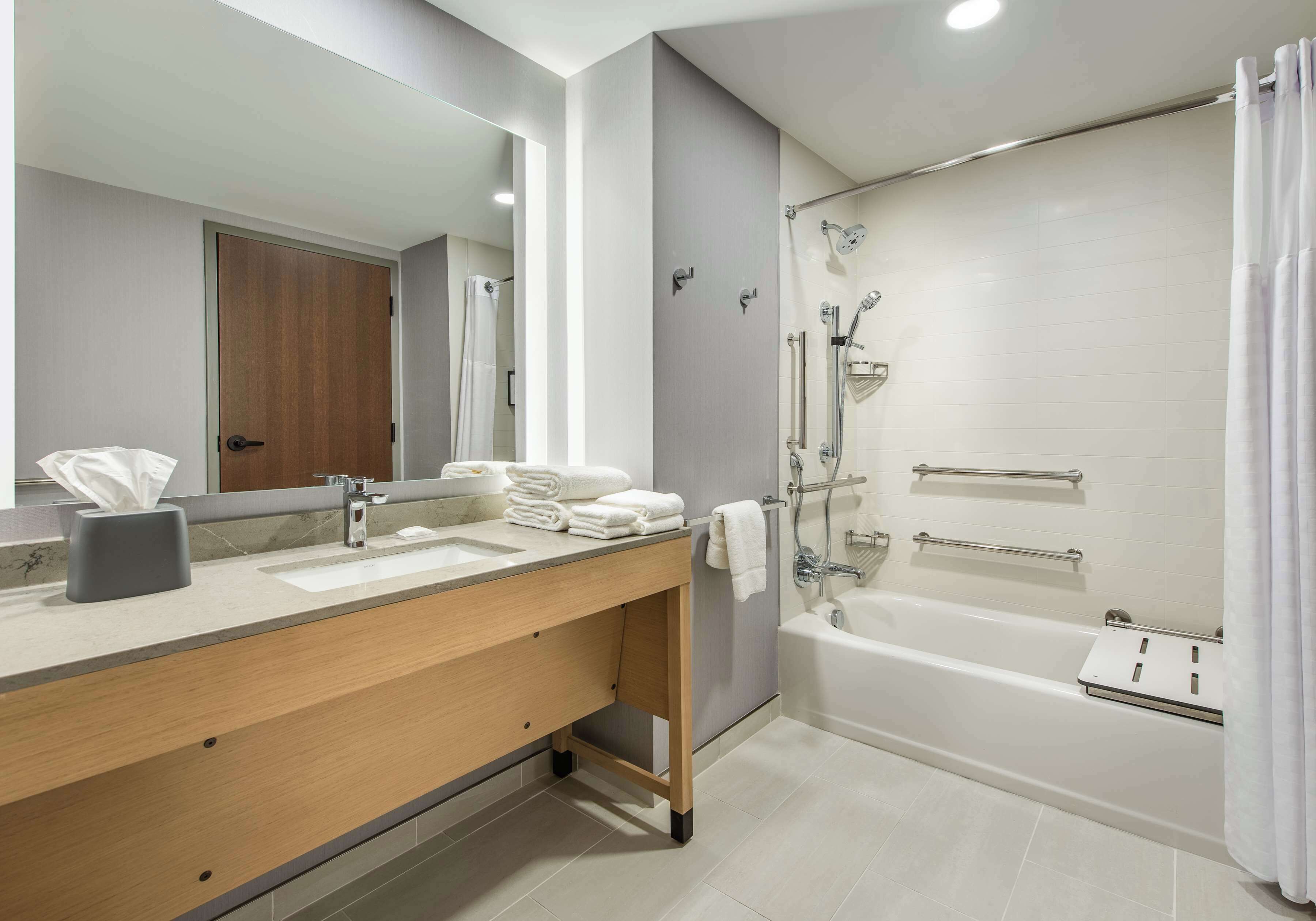 Un baño moderno con un espejo grande, un tocador de madera, una bañera y una ducha con puerta de vidrio.