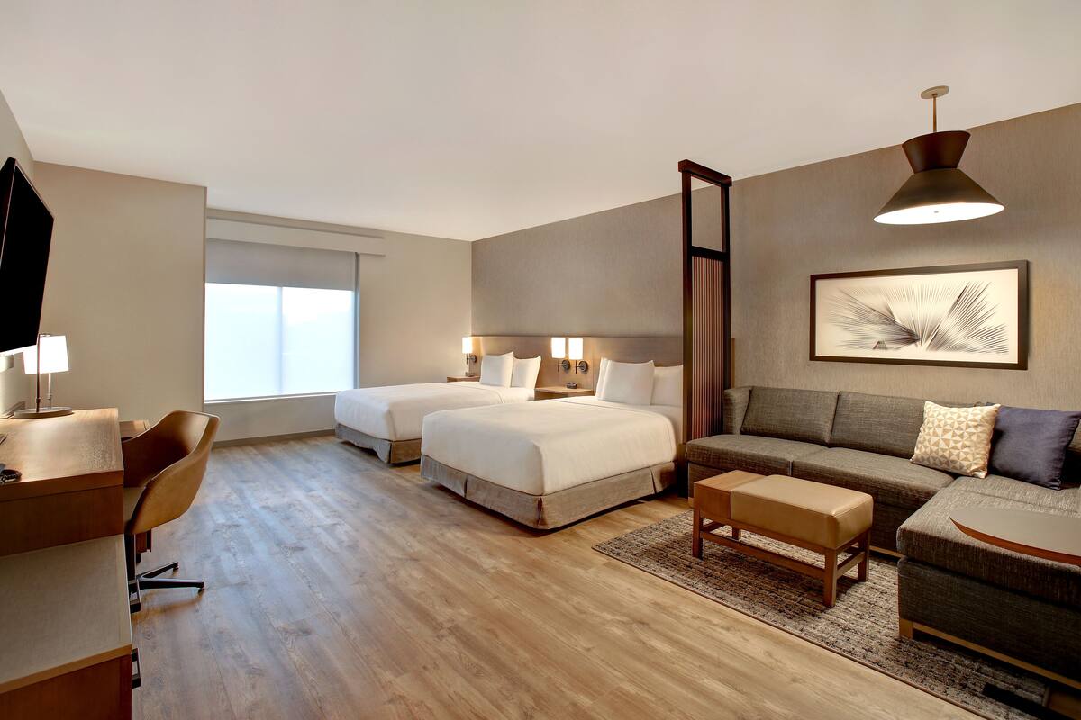 A hotel room with two beds, a sofa, a desk, and a large window.